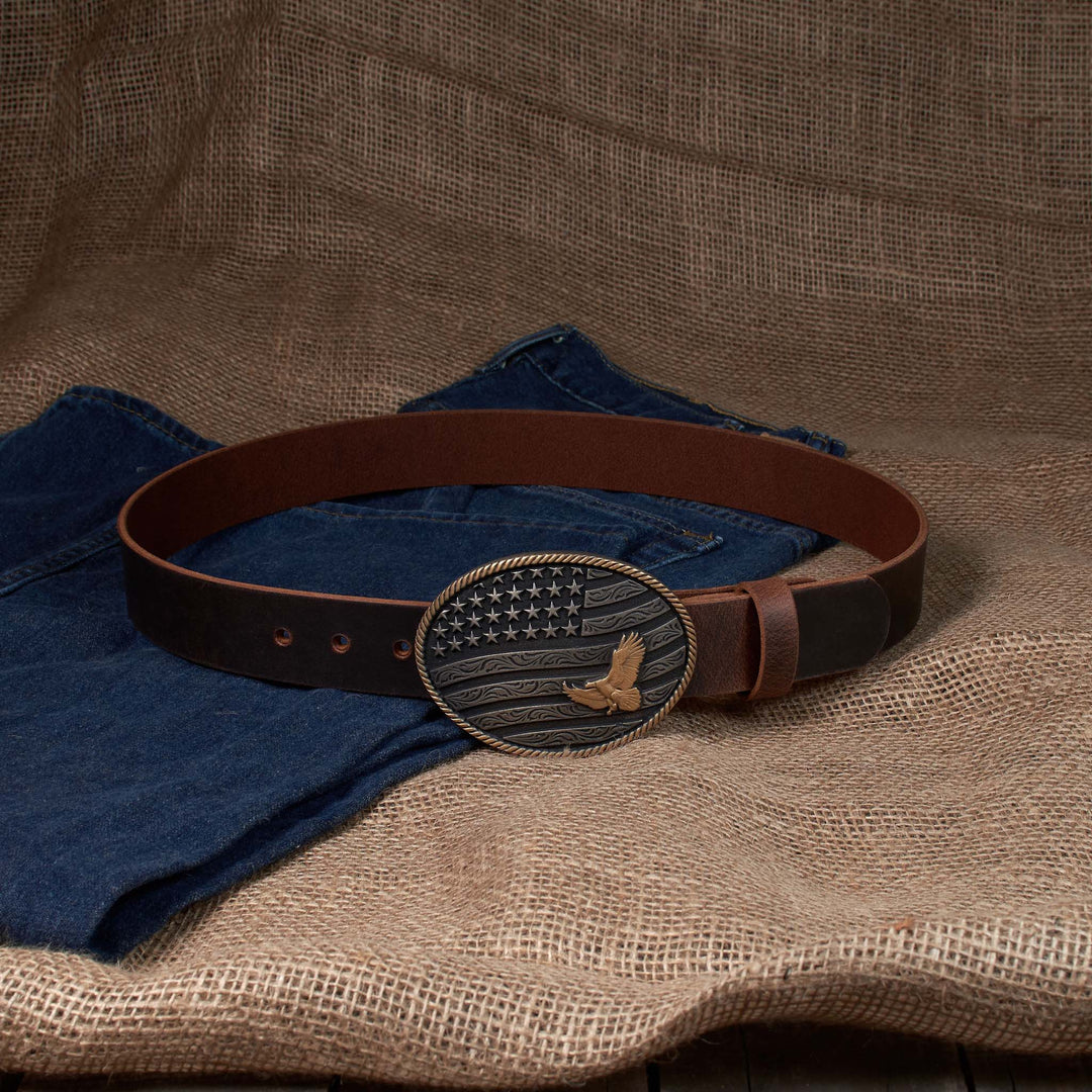 Brown leather belt with American flag buckle on blue jeans against a brown fabric background