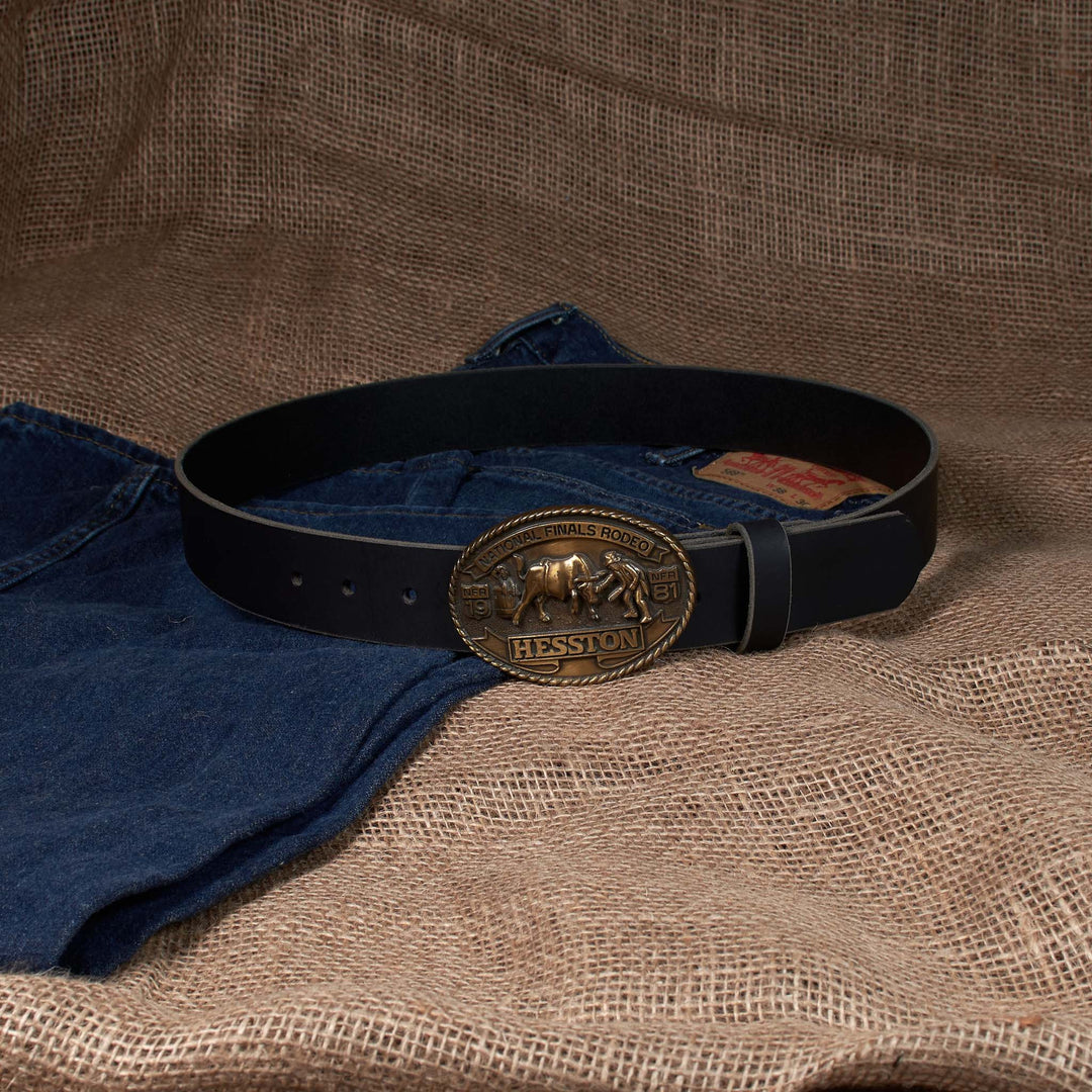 Black belt with a gold buckle on blue jeans against a brown fabric background