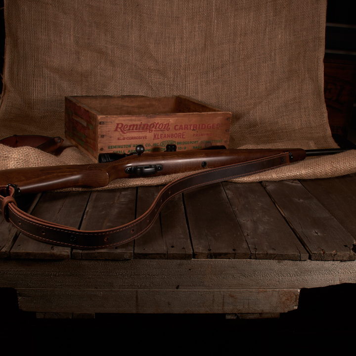Vintage rifle with leather stock on a wooden table, Remington cartridge box in the background.