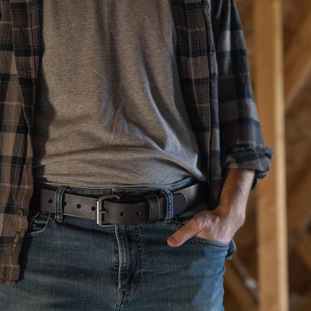 Person wearing a plaid shirt over a gray t-shirt with jeans, standing in a wooden framed room.