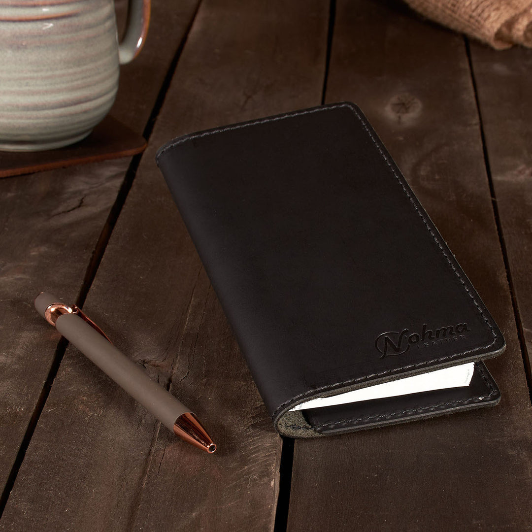 Black leather checkbook cover with a pen on a wooden surface