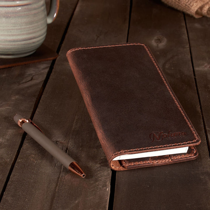 Brown leather checkbook cover with pen on a wooden surface