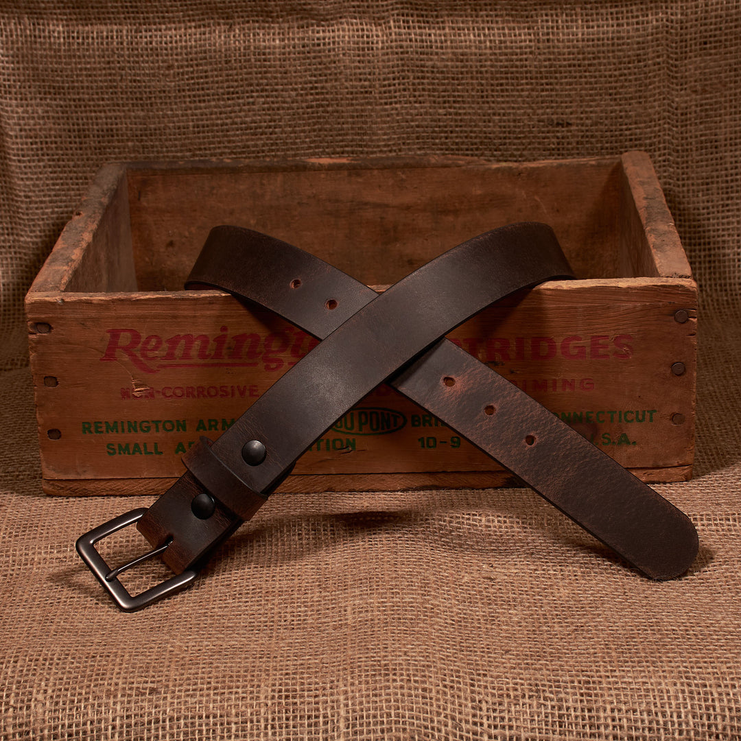 Brown leather belt with metal buckle on a wooden box labeled 'Remington'.