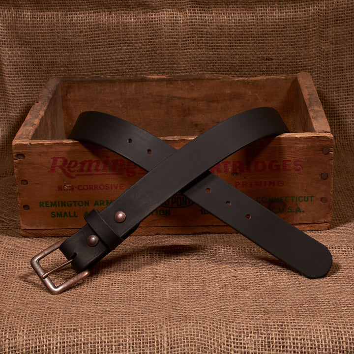 Black leather belt with a silver buckle on a rustic wooden box and burlap background