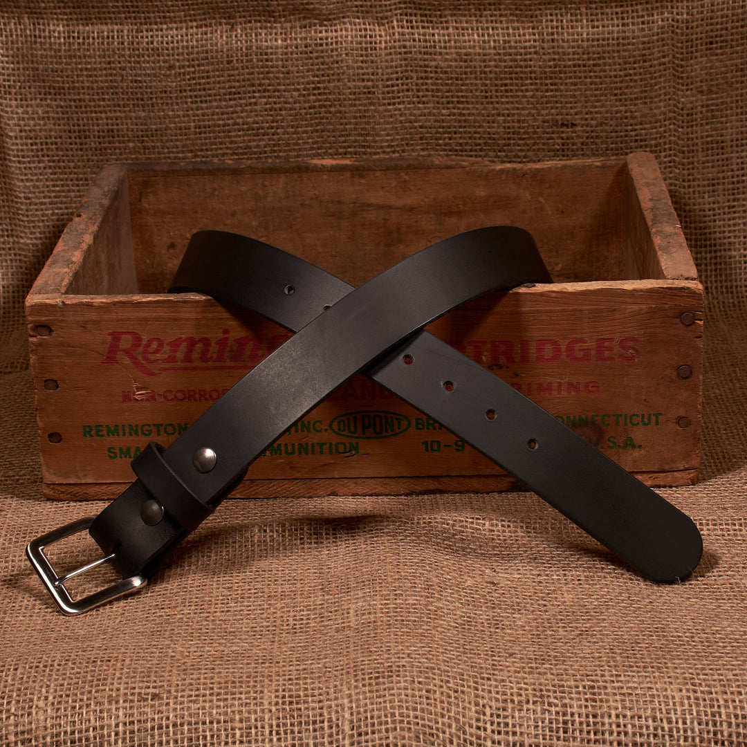 Black leather belt with silver buckle on a wooden crate with 'Remington' branding.