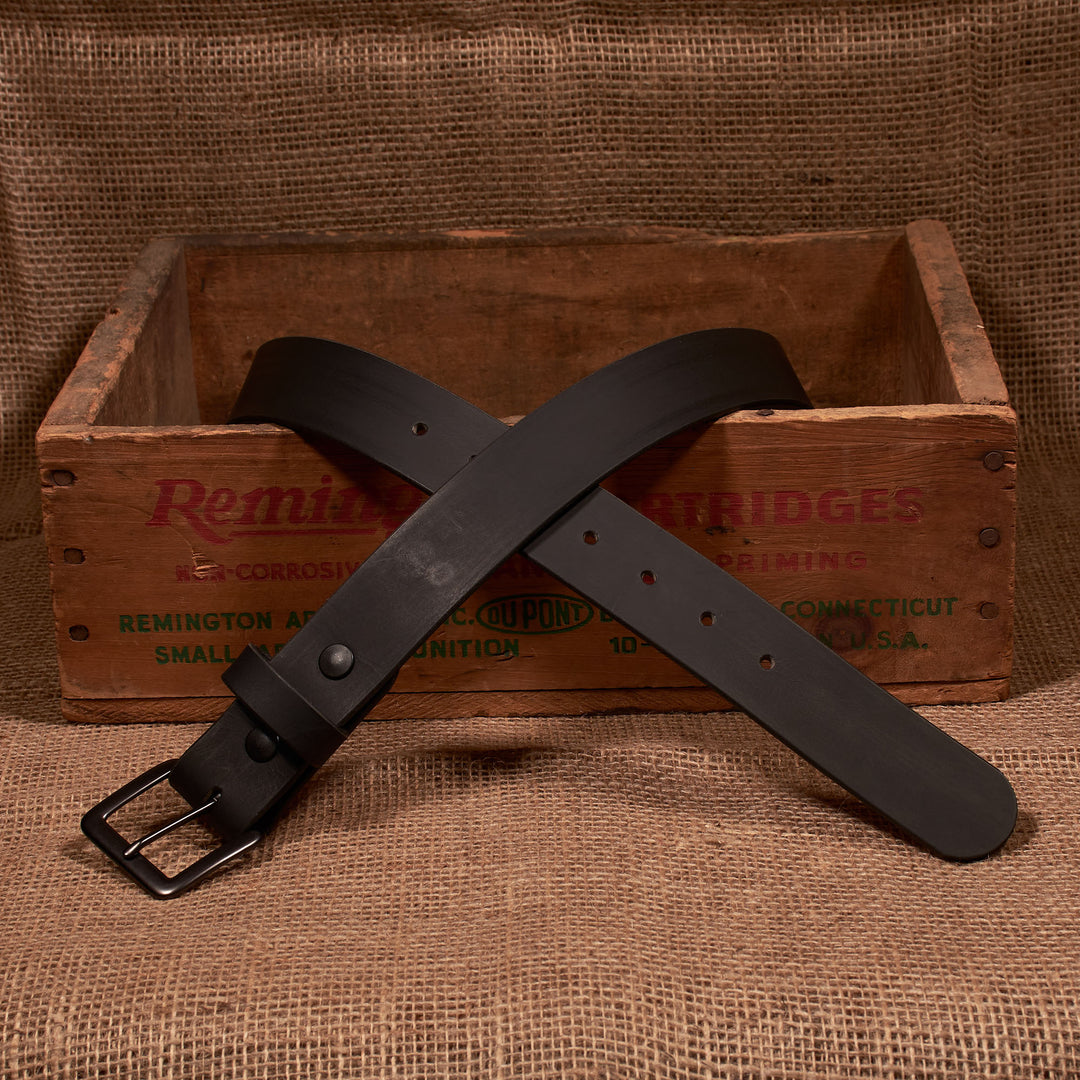 Black leather belt with a metal buckle on a rustic wooden crate background