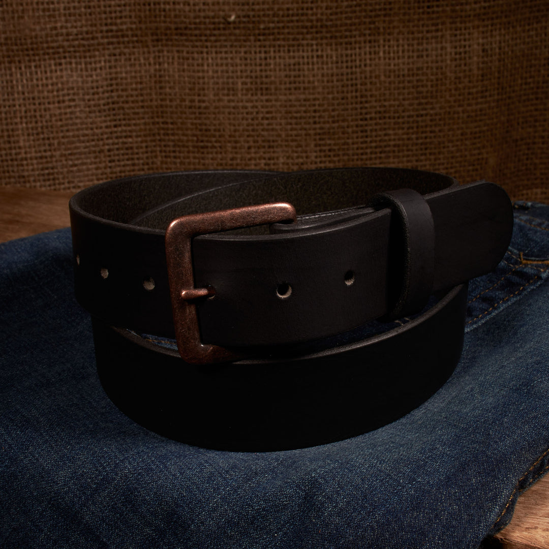 Black leather belt with a copper buckle on a denim surface.