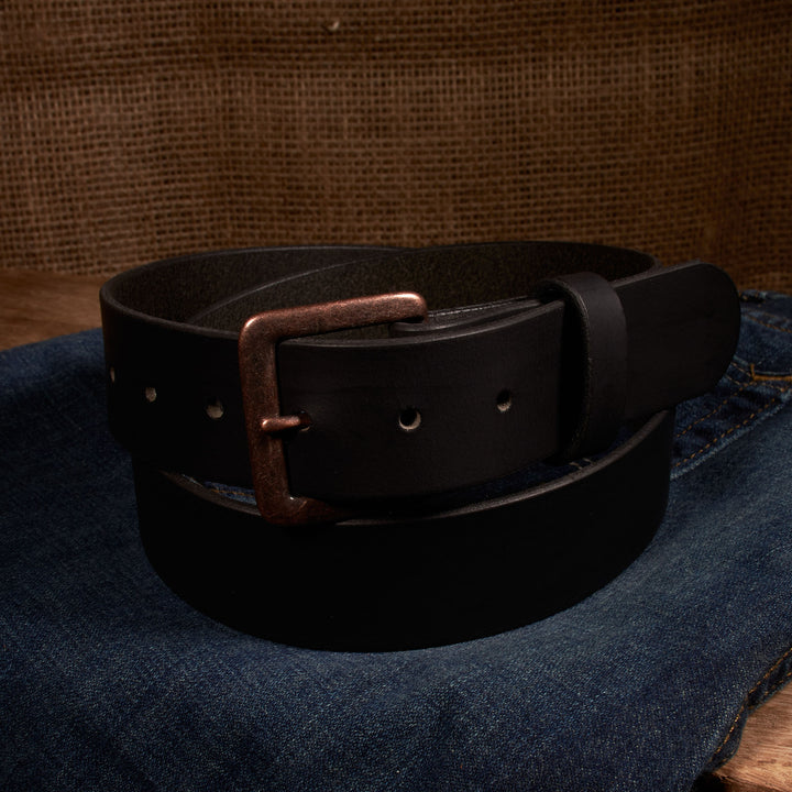 Black leather belt with a copper buckle on a denim surface.
