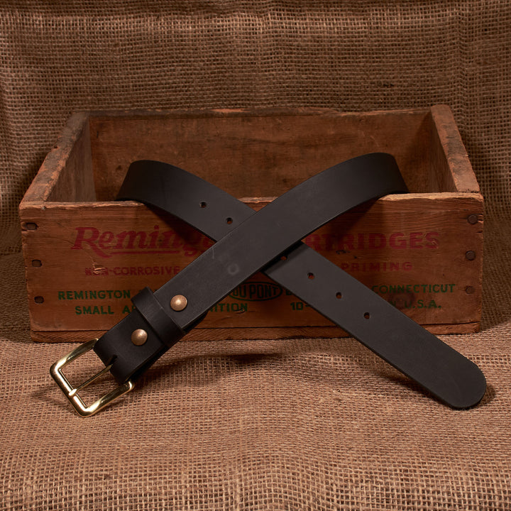 Black leather belt with brass buckle on a rustic wooden crate background