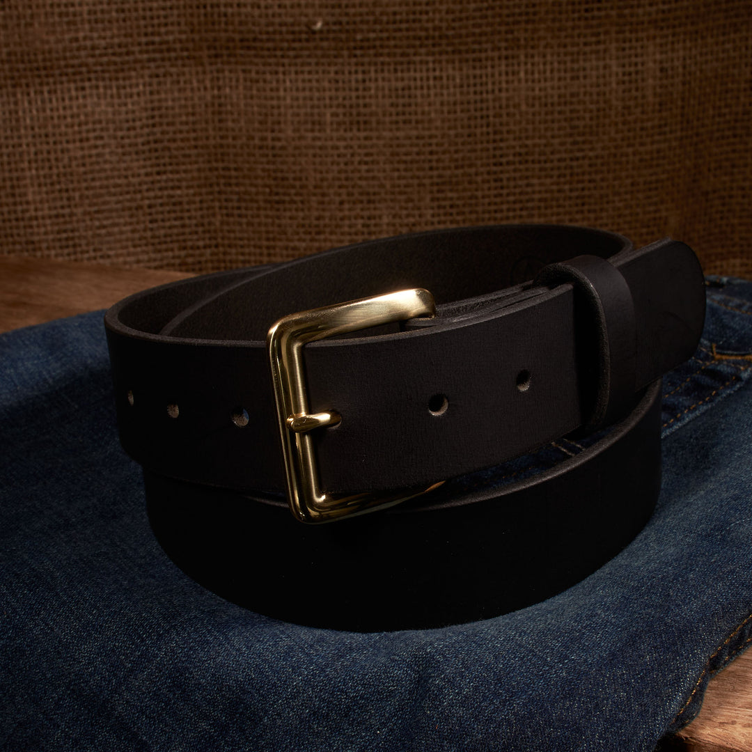 Black leather belt with a gold buckle on a denim surface.