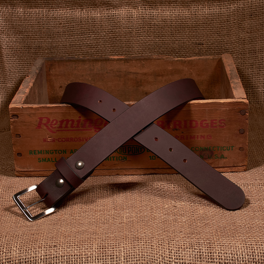 Brown leather belt with silver buckle on a rustic wooden box and burlap background