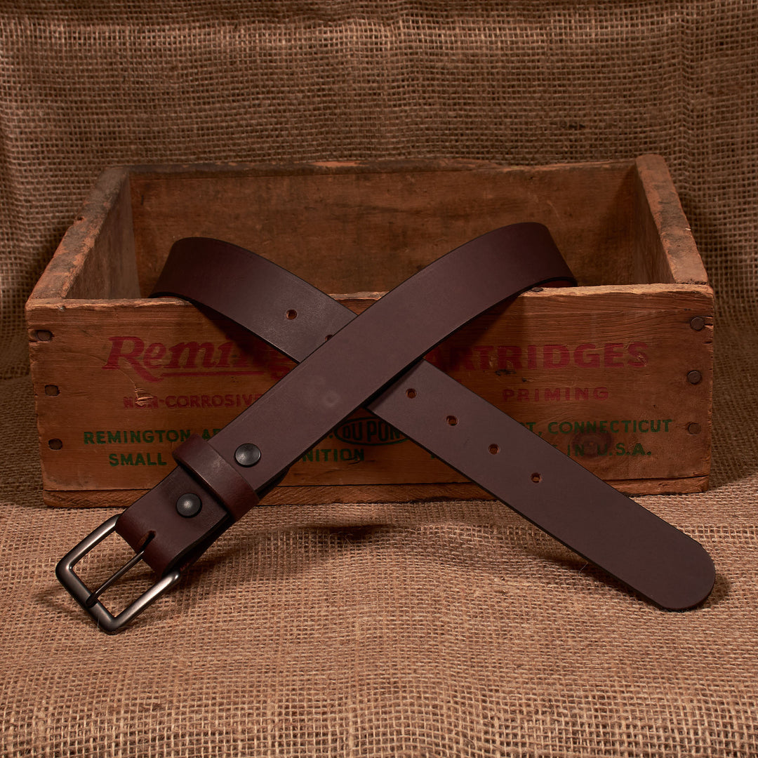 Brown leather belt with a silver buckle on a rustic wooden box background
