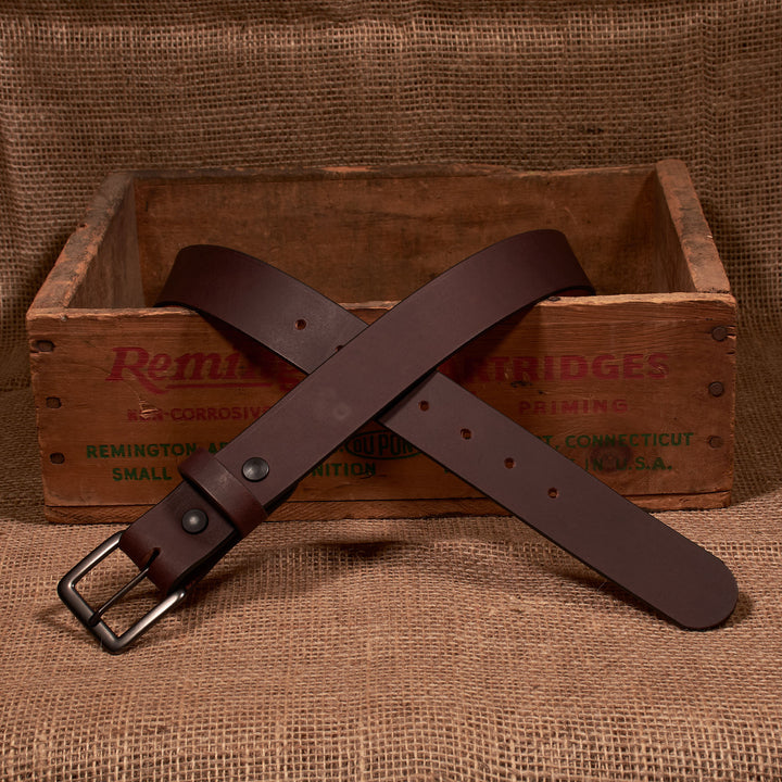 Brown leather belt with a silver buckle on a rustic wooden box background