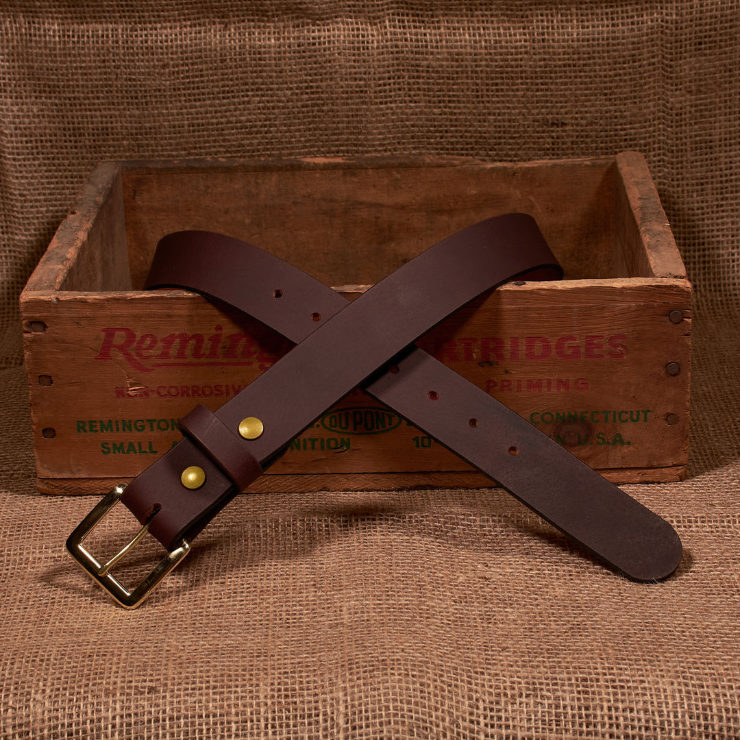 Brown leather belt with brass buckle on a wooden box labeled 'Remington'.