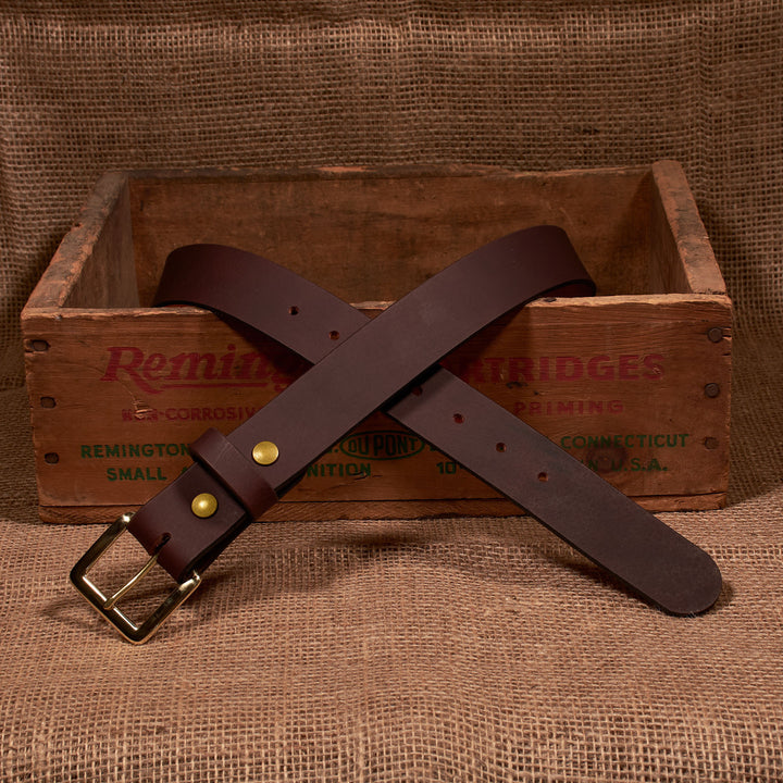 Brown leather belt with brass buckle on a wooden box labeled 'Remington'.