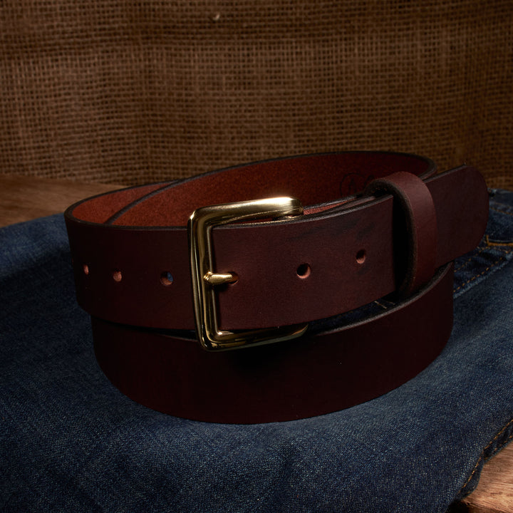 Brown leather belt with a gold buckle on a denim surface