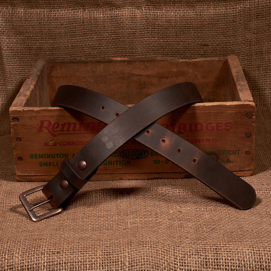 Brown leather belt with a metal buckle on a rustic wooden box and burlap background