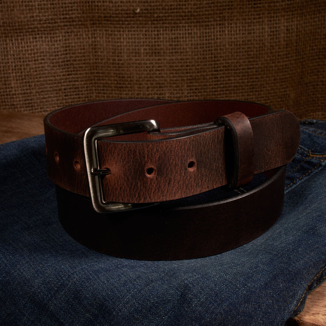 Brown leather belt with a silver buckle on a denim surface