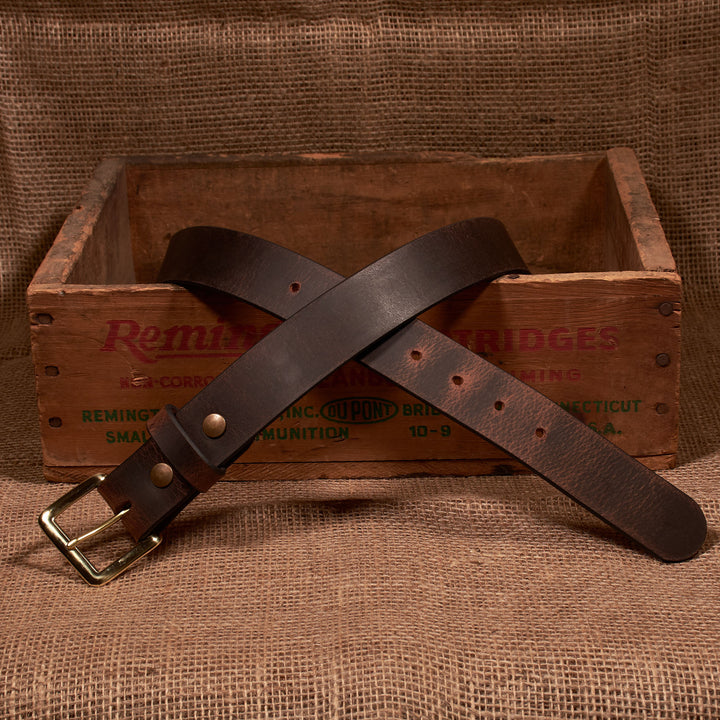Brown leather belt with brass buckle on a wooden box with 'Remington' branding.