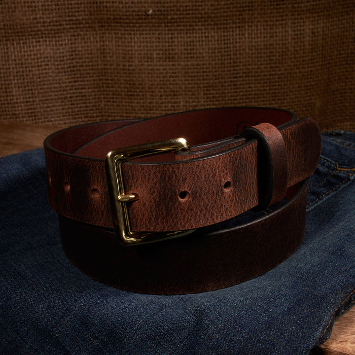 Brown leather belt with brass buckle on a denim surface
