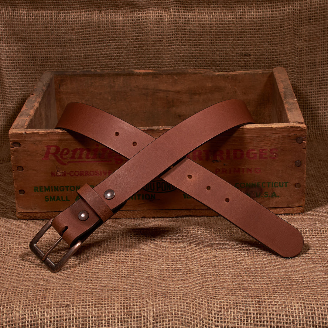 Brown leather belt with metal buckle on a wooden crate with 'Remington' branding.