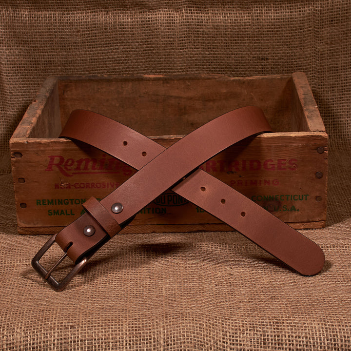 Brown leather belt with metal buckle on a wooden crate with 'Remington' branding.