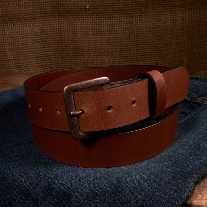 Brown leather belt with a brass buckle on a denim surface