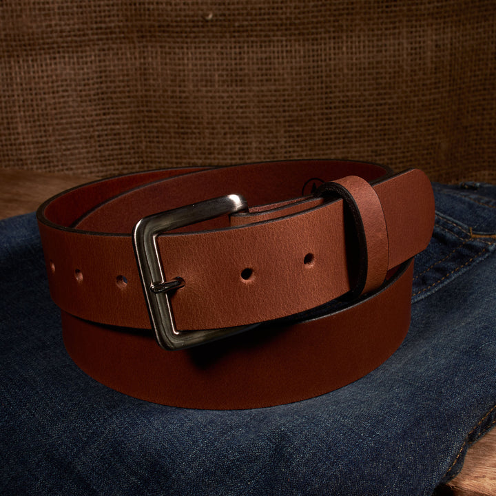 Brown leather belt with a silver buckle on blue jeans against a brown background