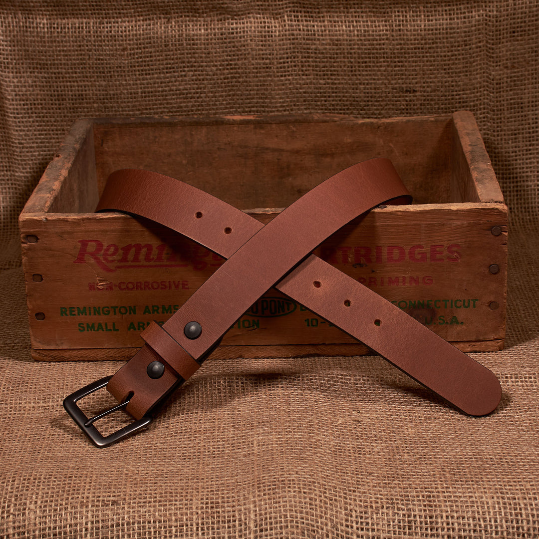 Brown leather belt with a black buckle on a wooden box labeled 'Remington'.