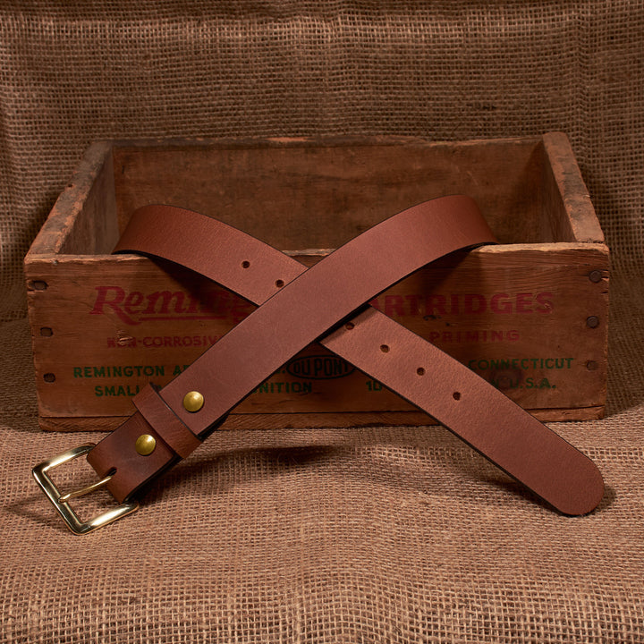 Brown leather belt with brass buckle on a wooden crate with 'Remington' branding.