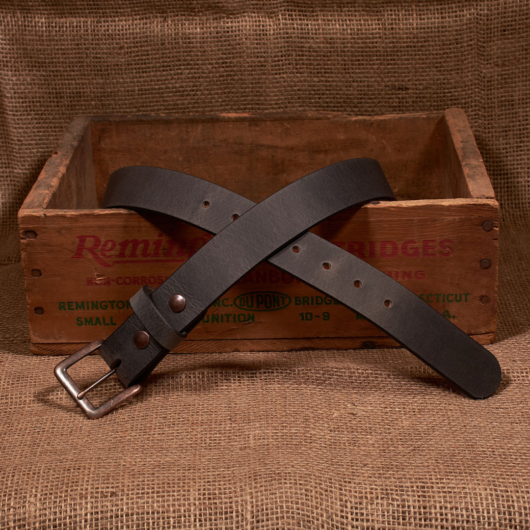 Brown leather belt with a silver buckle on a rustic wooden box and burlap background