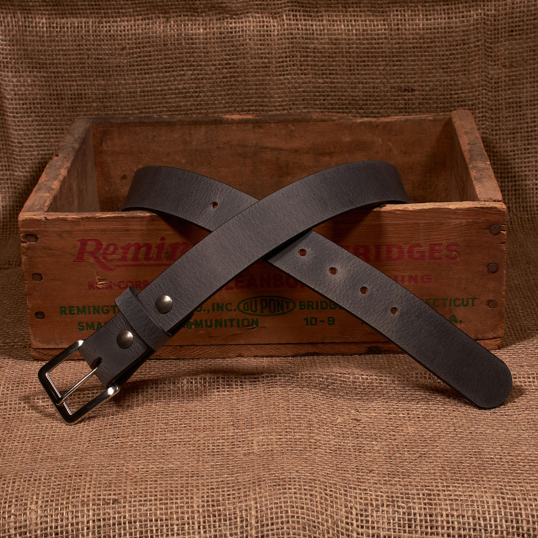 Brown leather belt with silver buckle on a wooden crate with 'Remington' branding.