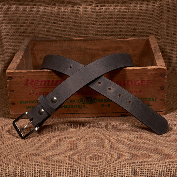 Brown leather belt with silver buckle on a wooden crate with 'Remington' branding.