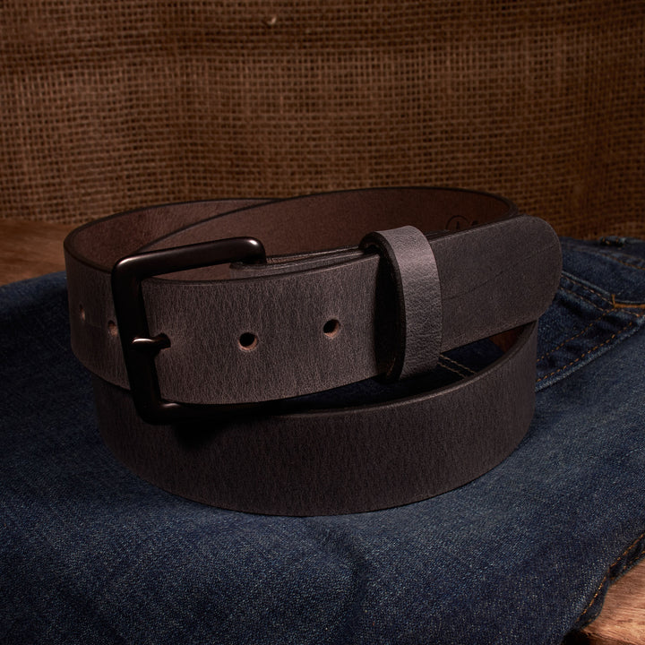 Brown leather belt with a black buckle on a denim surface.