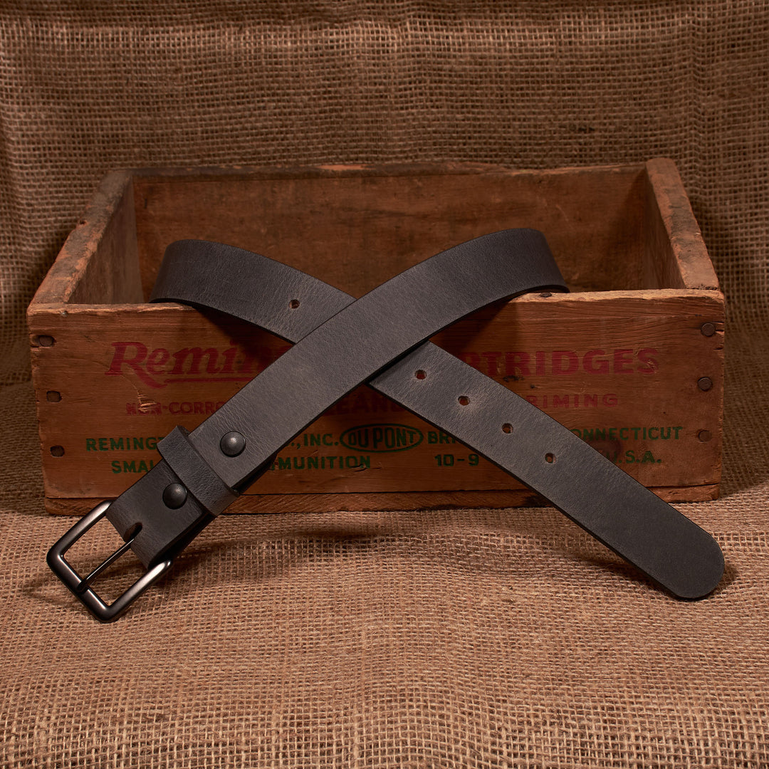 Brown leather belt with a buckle on a wooden crate with 'Remington' branding.