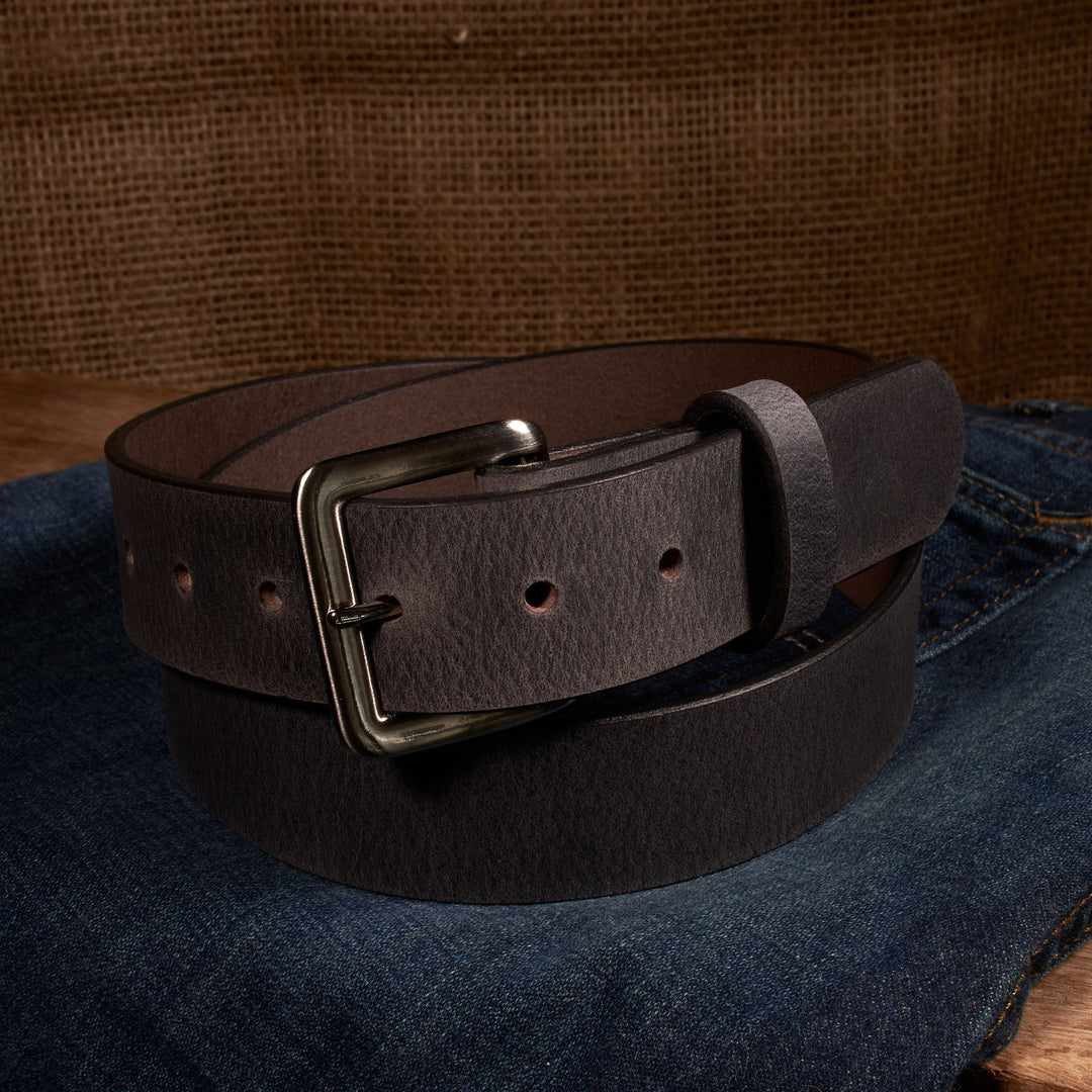 Brown leather belt with a silver buckle on a denim surface.