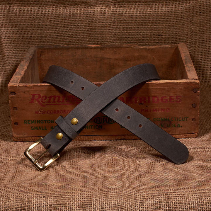 Brown leather belt with brass buckle on a wooden crate labeled 'Remington Bridges'.