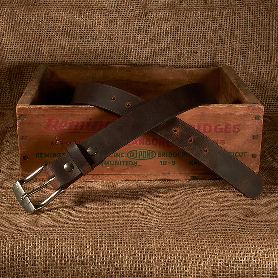 Brown leather belt with silver buckle on a wooden crate with 'Remington' branding.