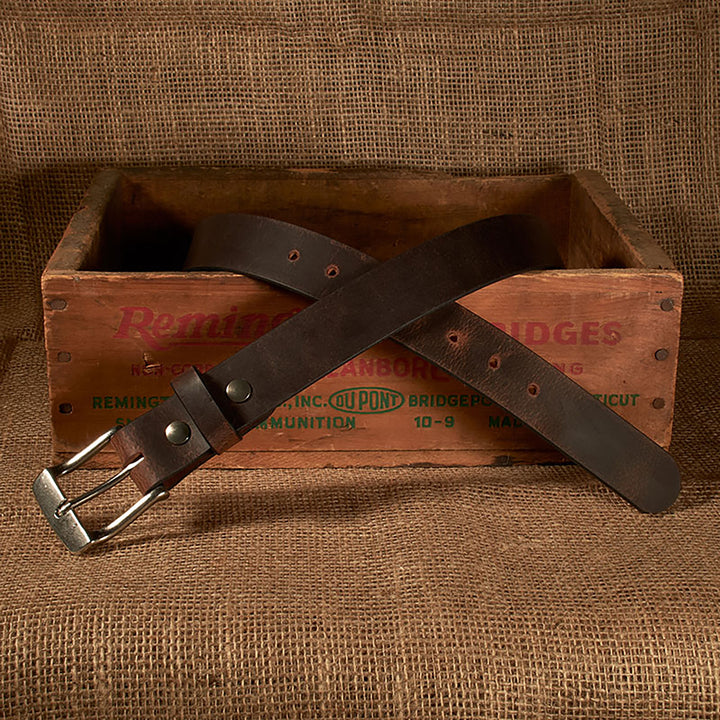 Brown leather belt with silver buckle on a wooden crate with 'Remington' branding.