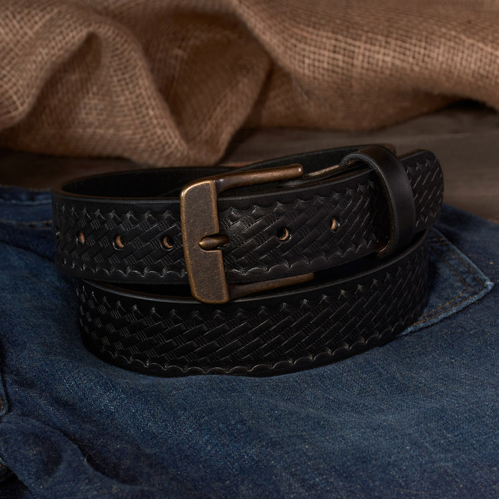 Black leather belt with a brass buckle on blue jeans against a brown fabric background