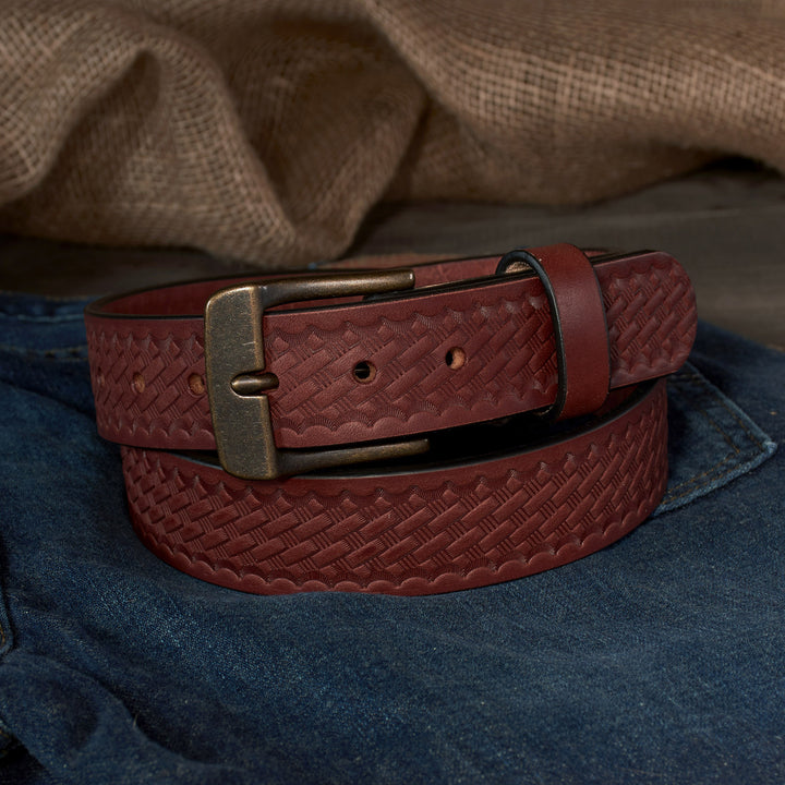 Brown leather belt with a basketweave pattern and brass buckle on a denim surface.