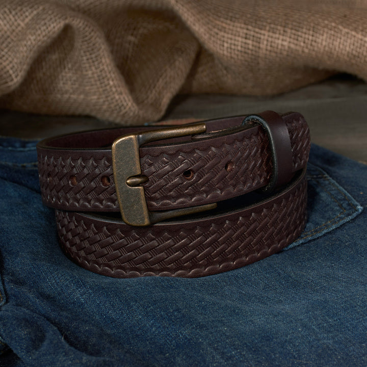 Brown basketweave leather belt with a brass buckle on blue denim fabric.