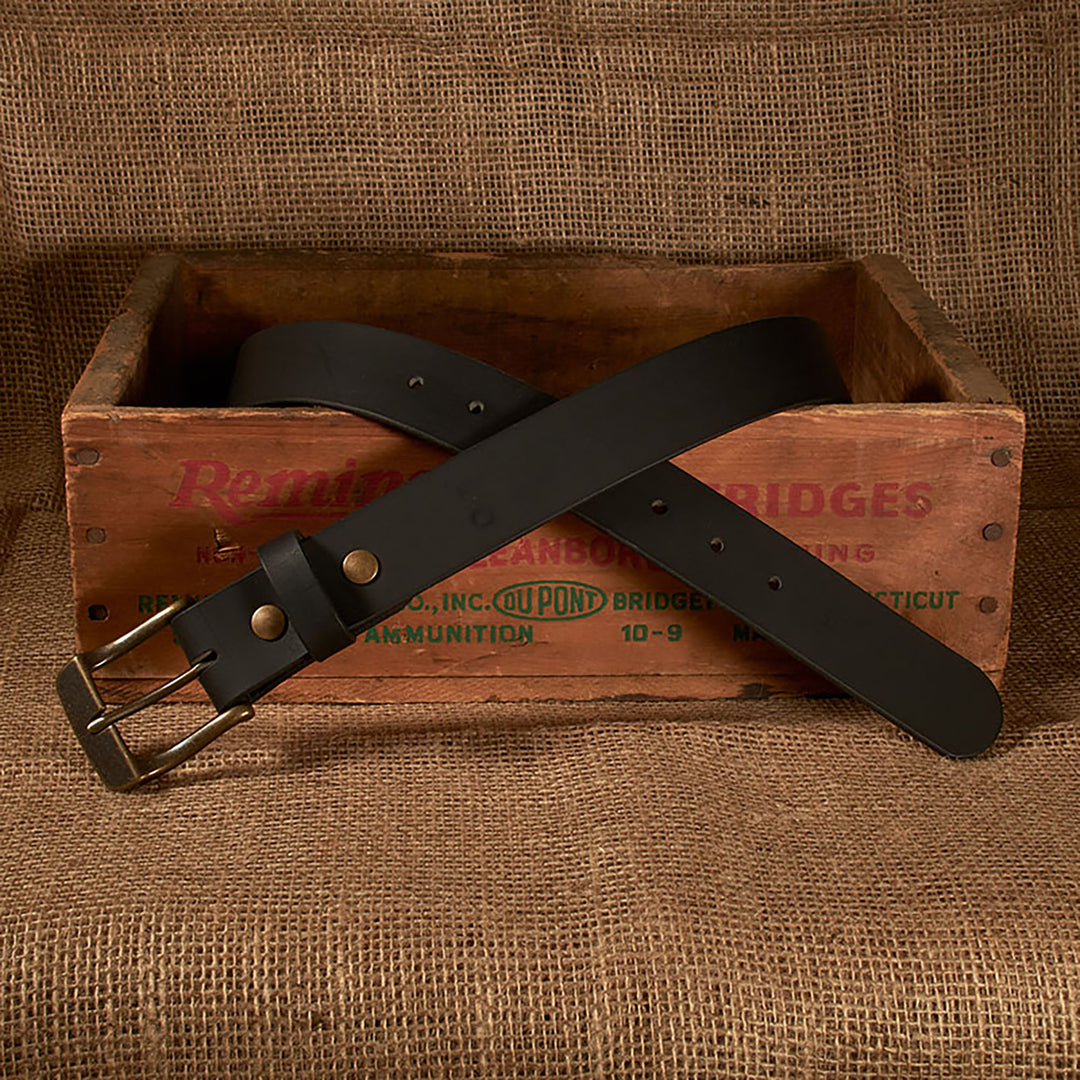 Black belt with brass buckle on a wooden crate with 'Remington' branding.