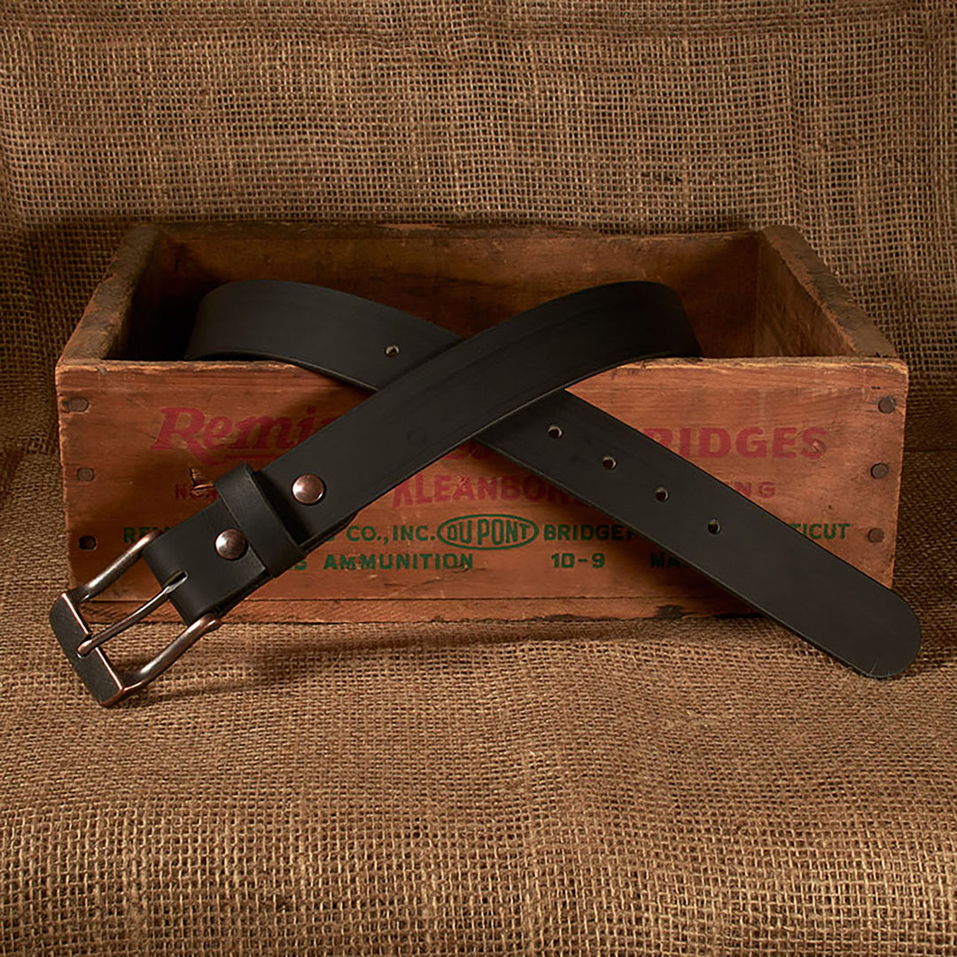 Black belt with silver buckle on a rustic wooden box against a burlap background