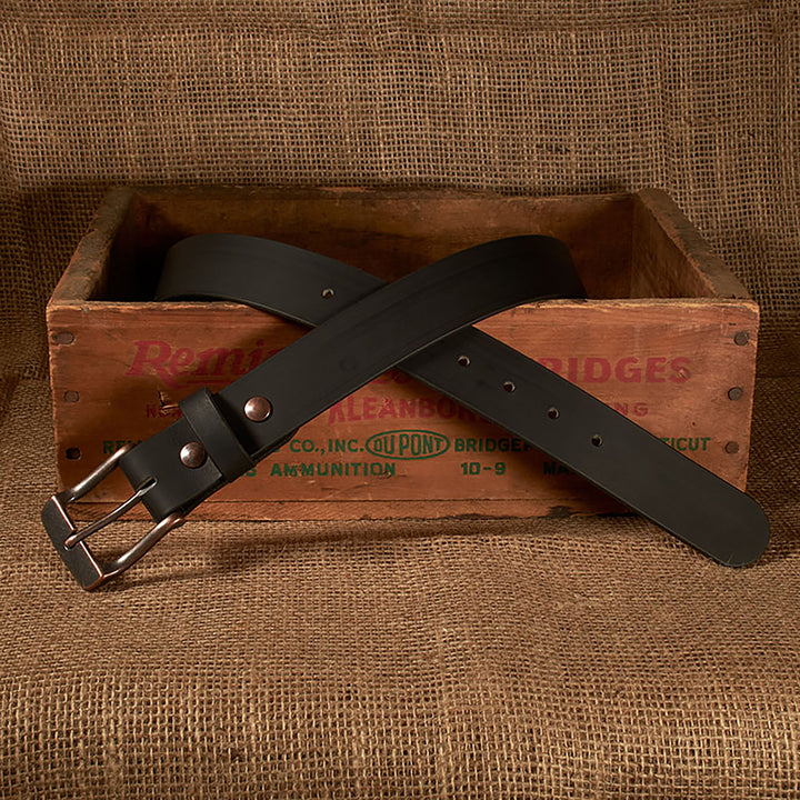 Black belt with silver buckle on a rustic wooden box against a burlap background