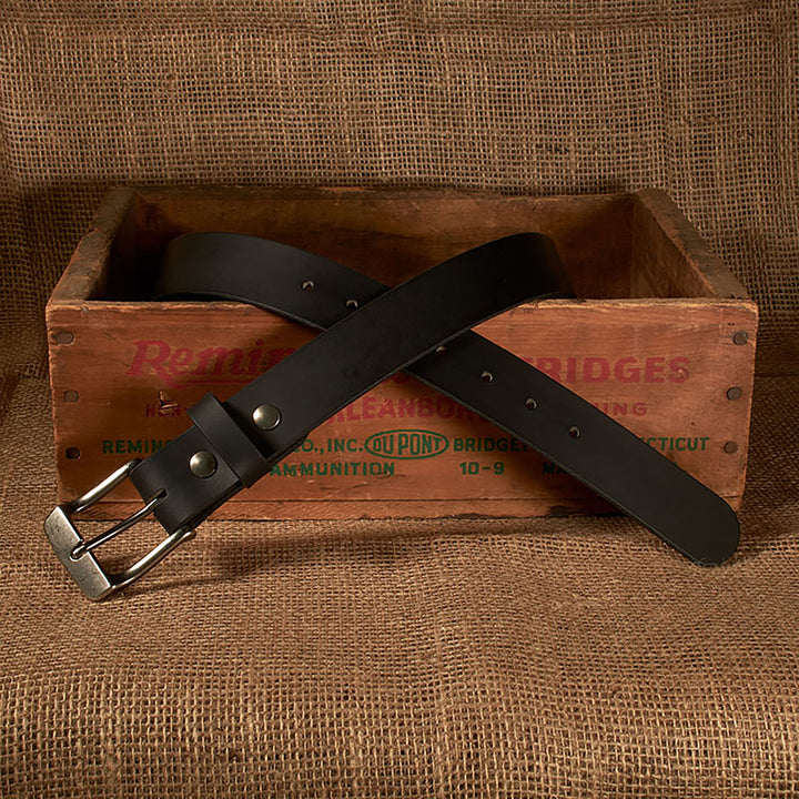 Black belt with silver buckle on a wooden crate against a brown fabric background