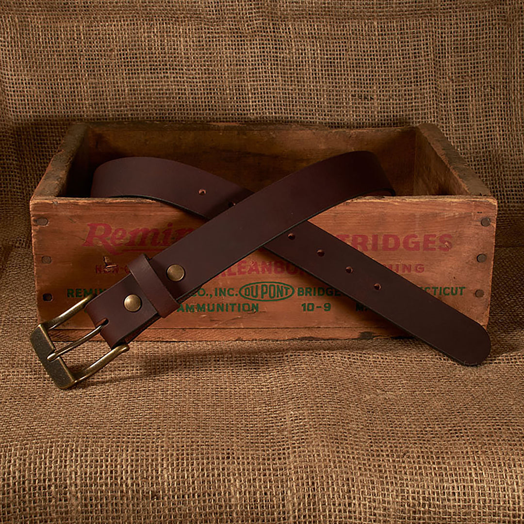 Brown leather belt with brass buckle on a wooden box with 'Remington' branding.
