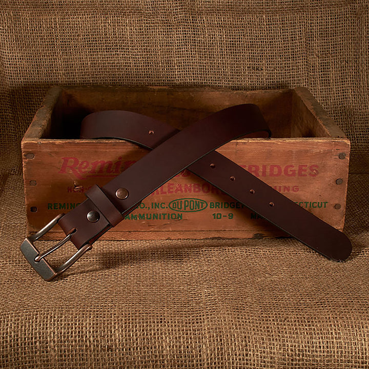 Brown leather belt with silver buckle on a rustic wooden crate against a burlap background