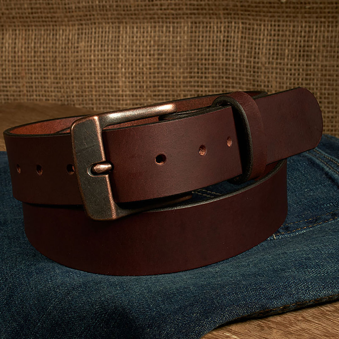 Brown leather belt with a brass buckle on blue jeans against a brown fabric background