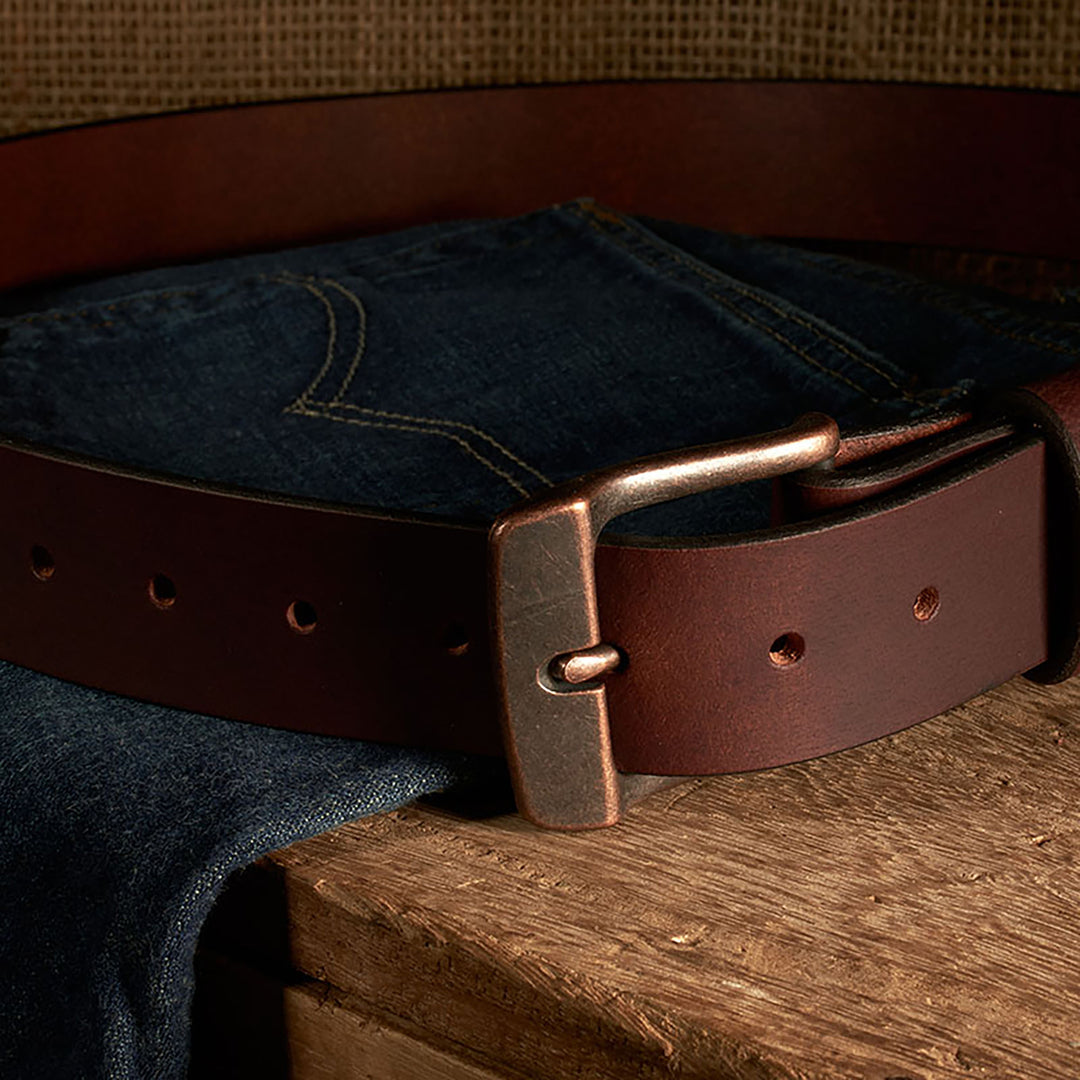 Dark blue jeans with a brown leather belt on a wooden surface